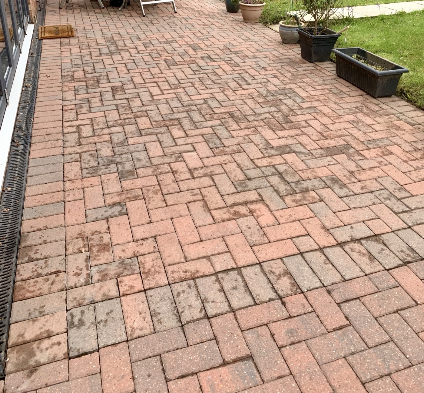 Block paved driveway during a pressure wash, one half still dark with grime, the other half restored to its original red